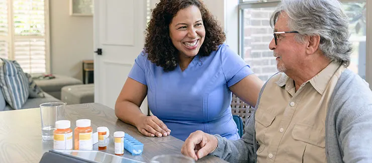 A caregiver reviewing medication bottles with an older man at a table